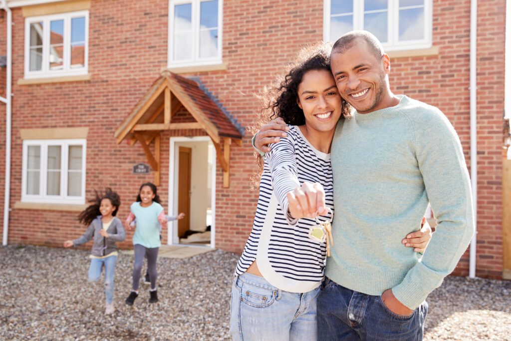 Happy couple holding house keys with children outside their new home after completing a home title search